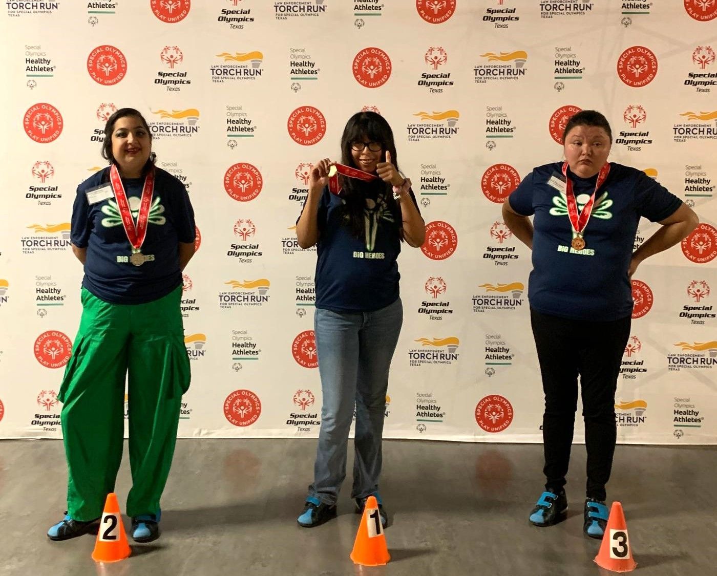 Three women standing in front of a wall with medals around their necks