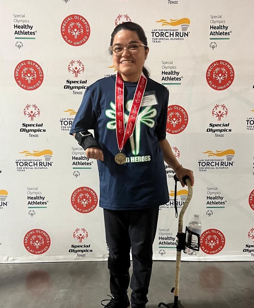 A woman wearing a medal and a cane is standing in front of a wall.