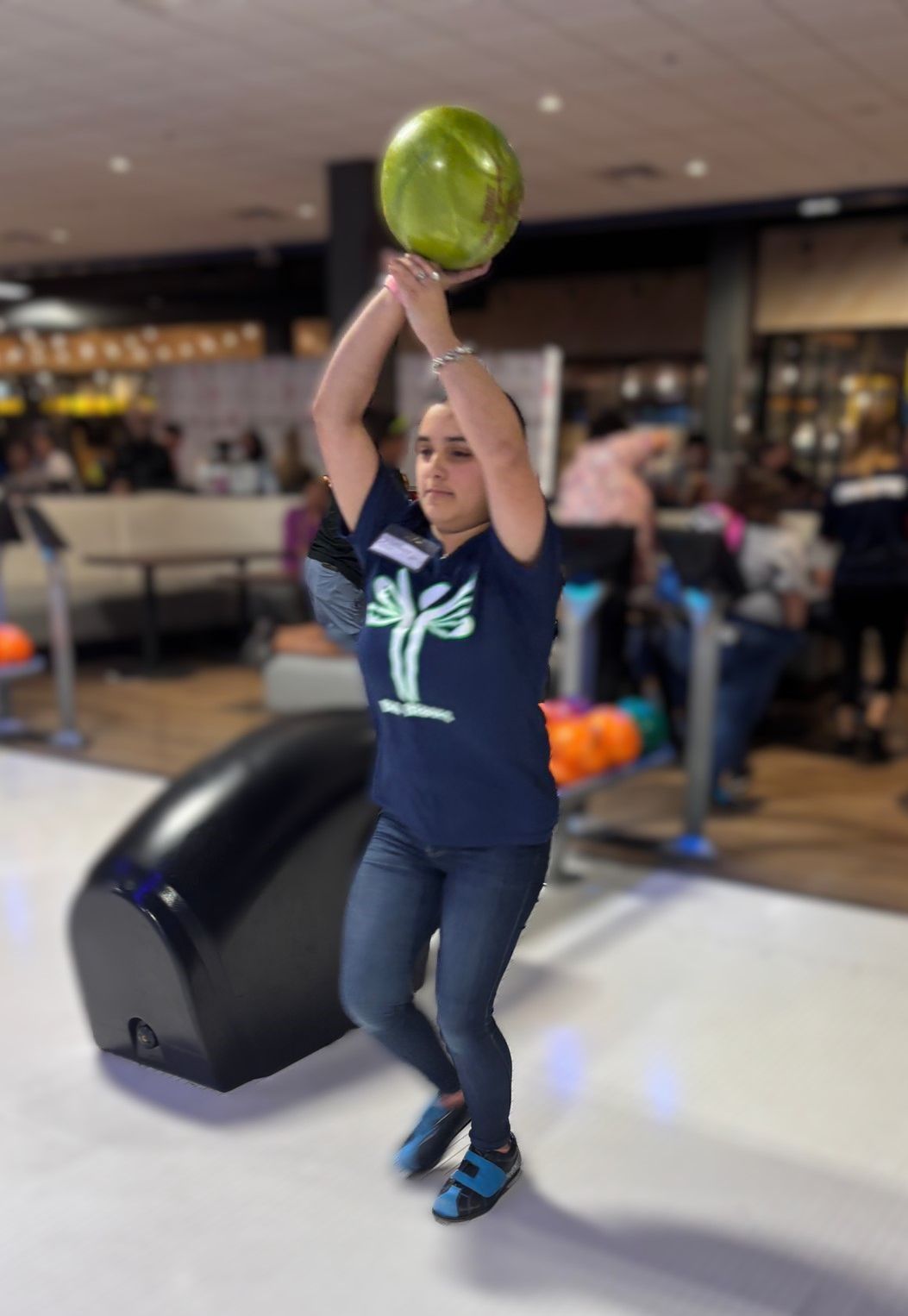 A woman in a blue shirt is throwing a bowling ball