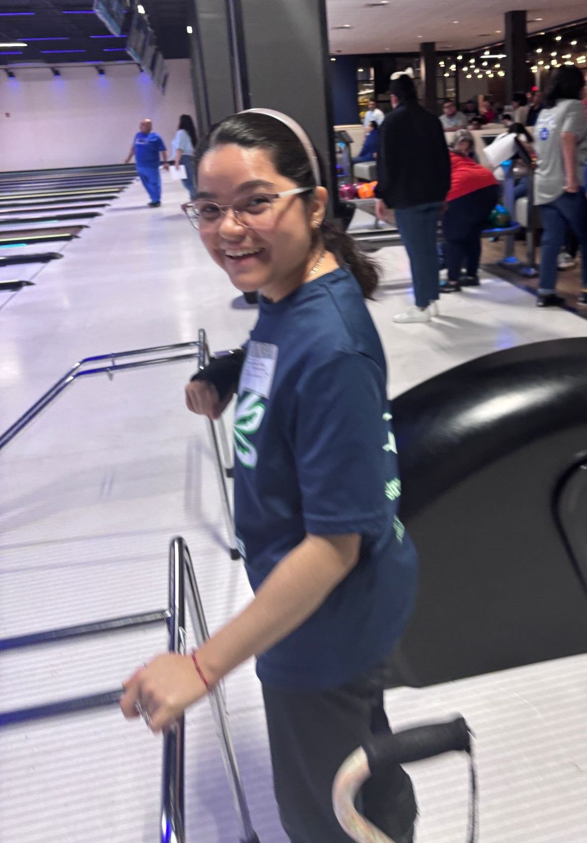A girl in a blue shirt is standing in a bowling alley.