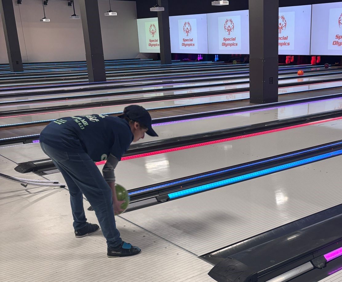 A man is bending over to pick up a bowling ball in a bowling alley