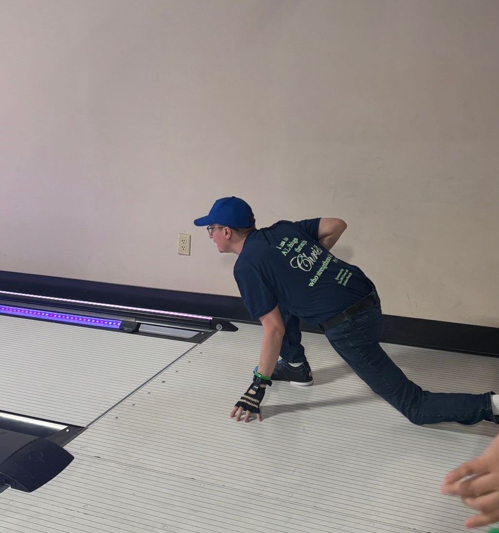 A man in a blue shirt with the word coca cola on the back is playing bowling