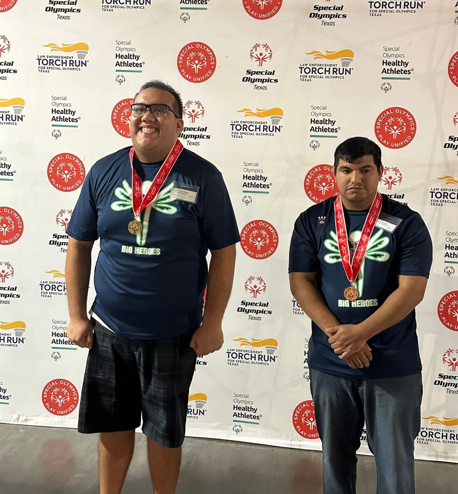 Two men wearing medals stand in front of a wall that says torch run