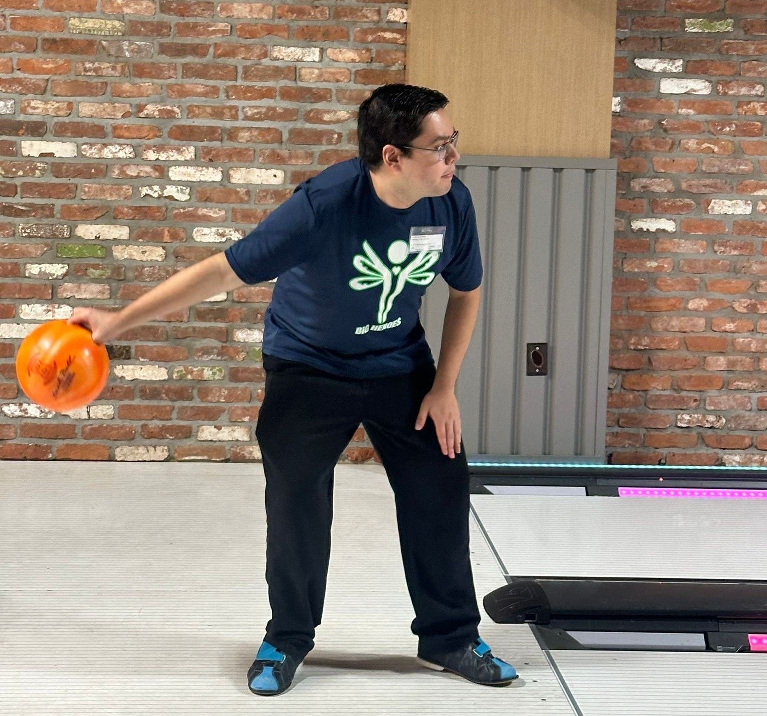 A man wearing a blue shirt with a green butterfly on it is throwing a bowling ball