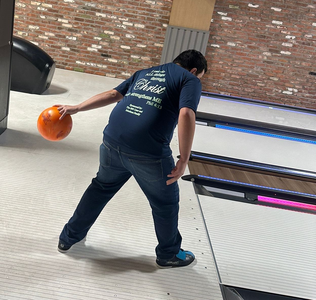 A man in a blue shirt is throwing a bowling ball