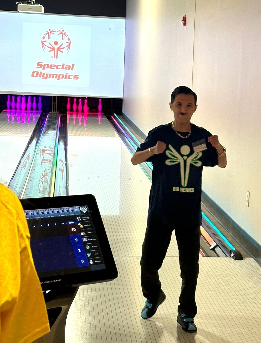 A boy in a special olympics shirt stands in a bowling alley