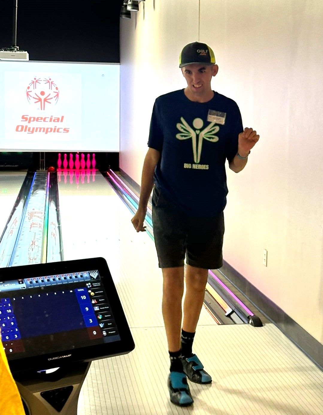 A man in a blue shirt with a dragonfly on it is standing in a bowling alley