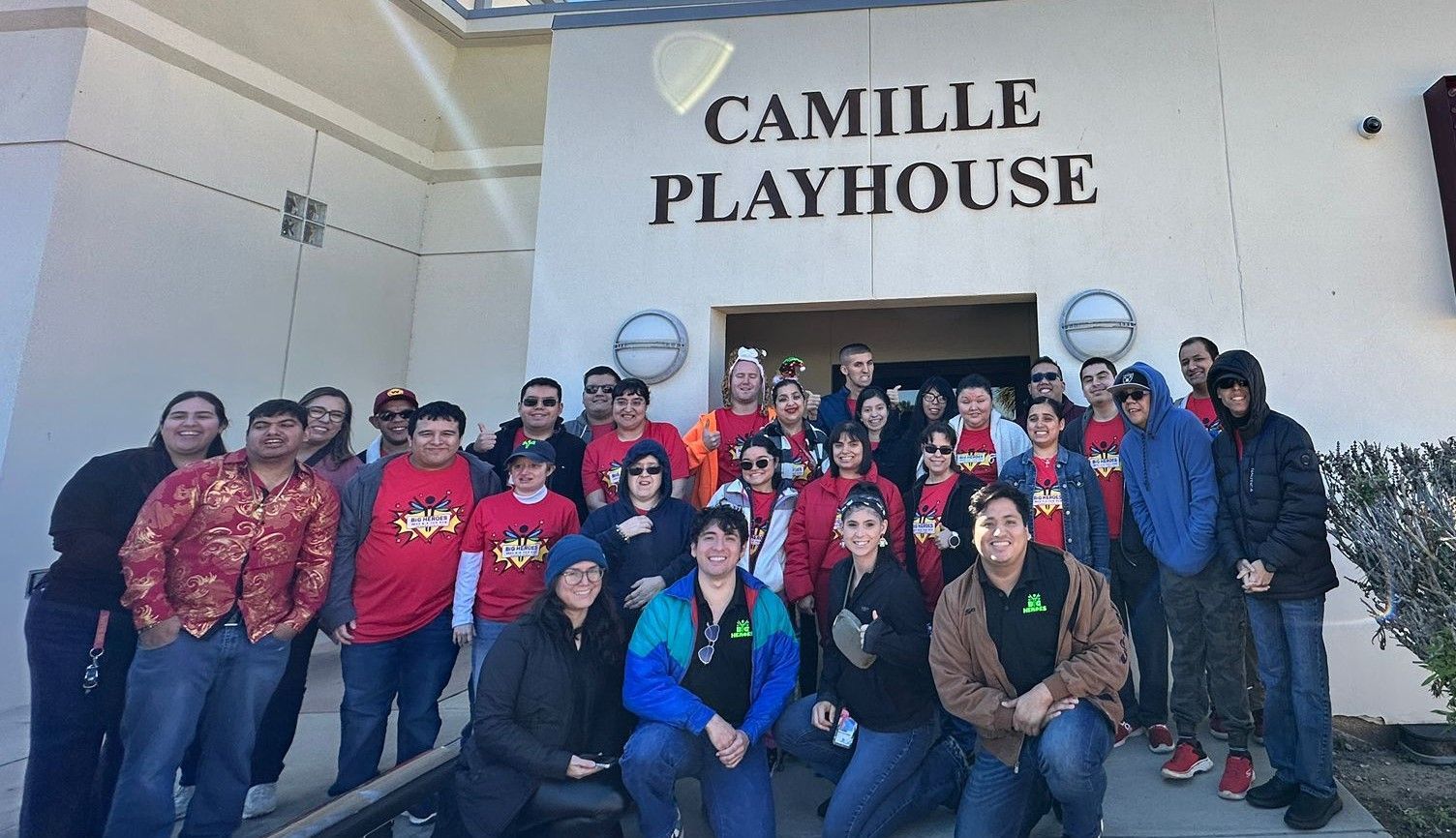 A group of people are posing for a picture in front of a building that says camille playhouse.