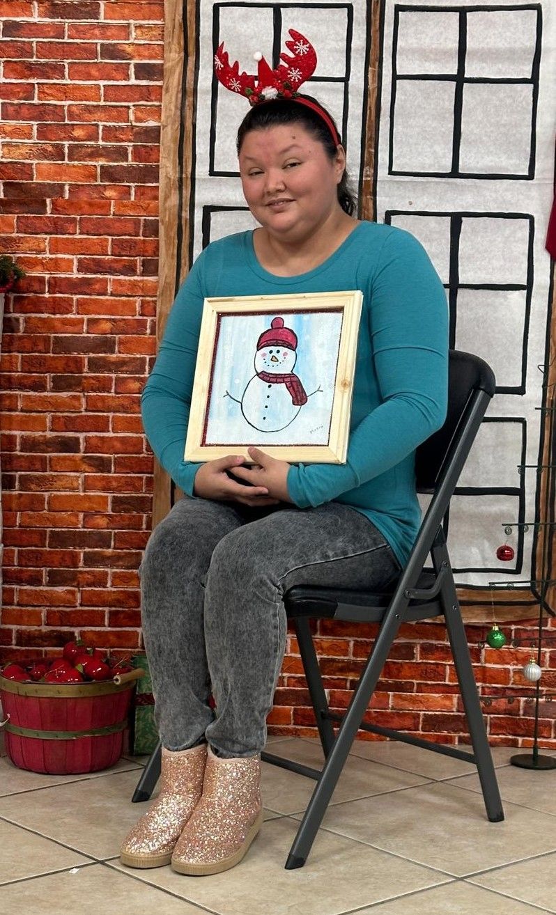 A woman is sitting in a chair holding a picture of a snowman.
