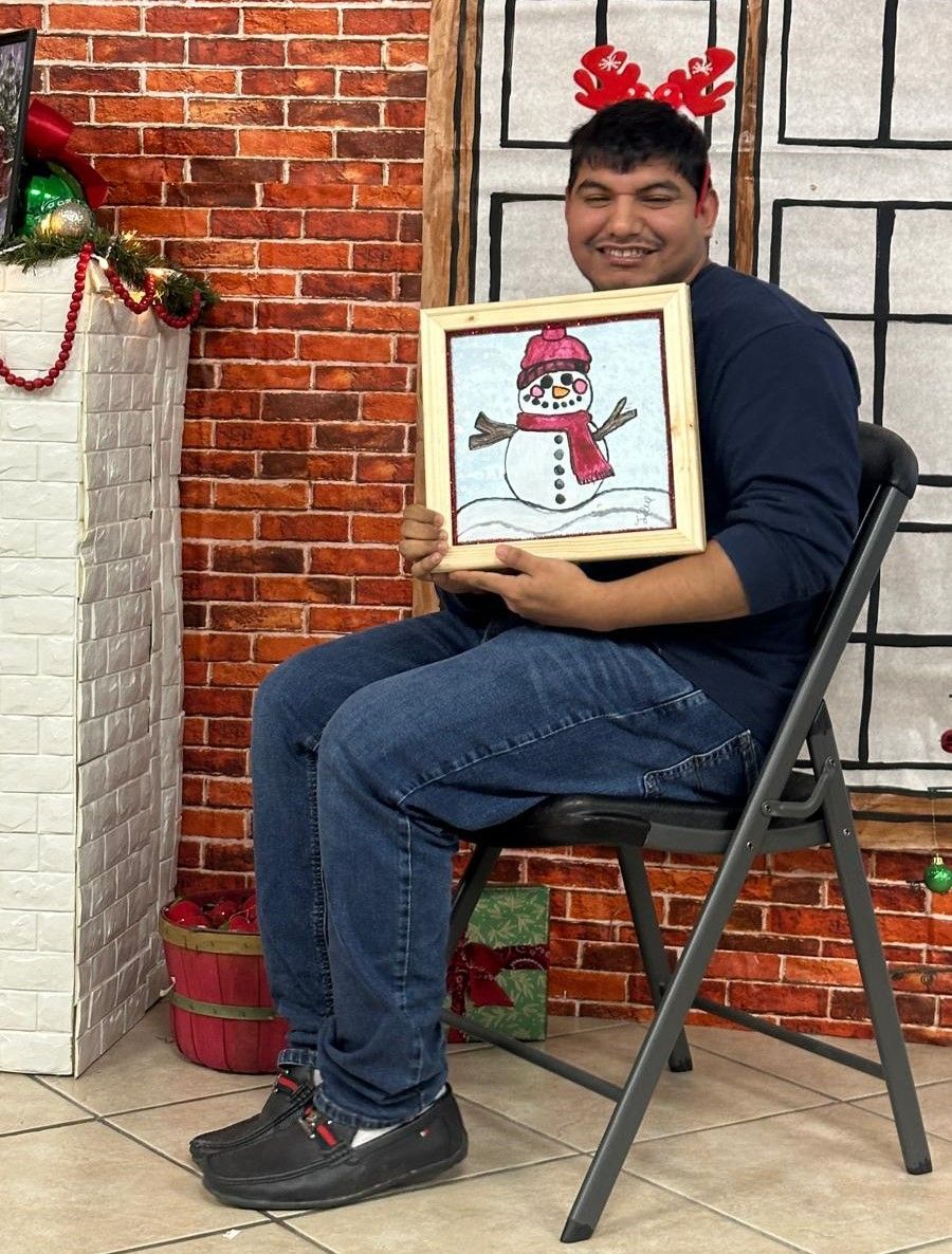 A man is sitting in a chair holding a picture of a snowman.