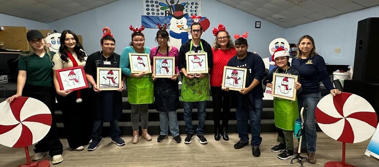 A group of people are standing in a room holding paintings.