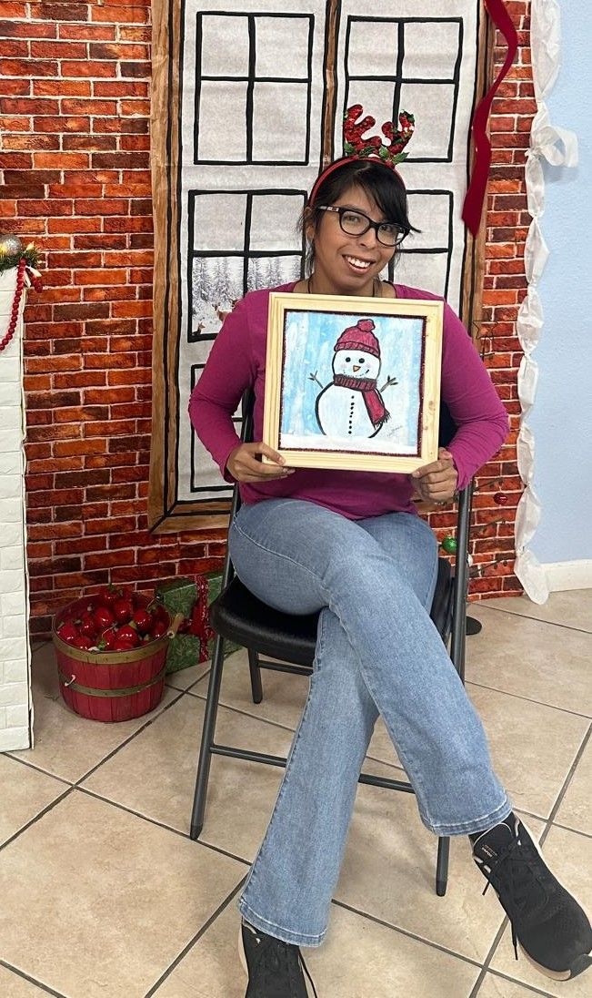 A woman is sitting in a chair holding a painting of a snowman.