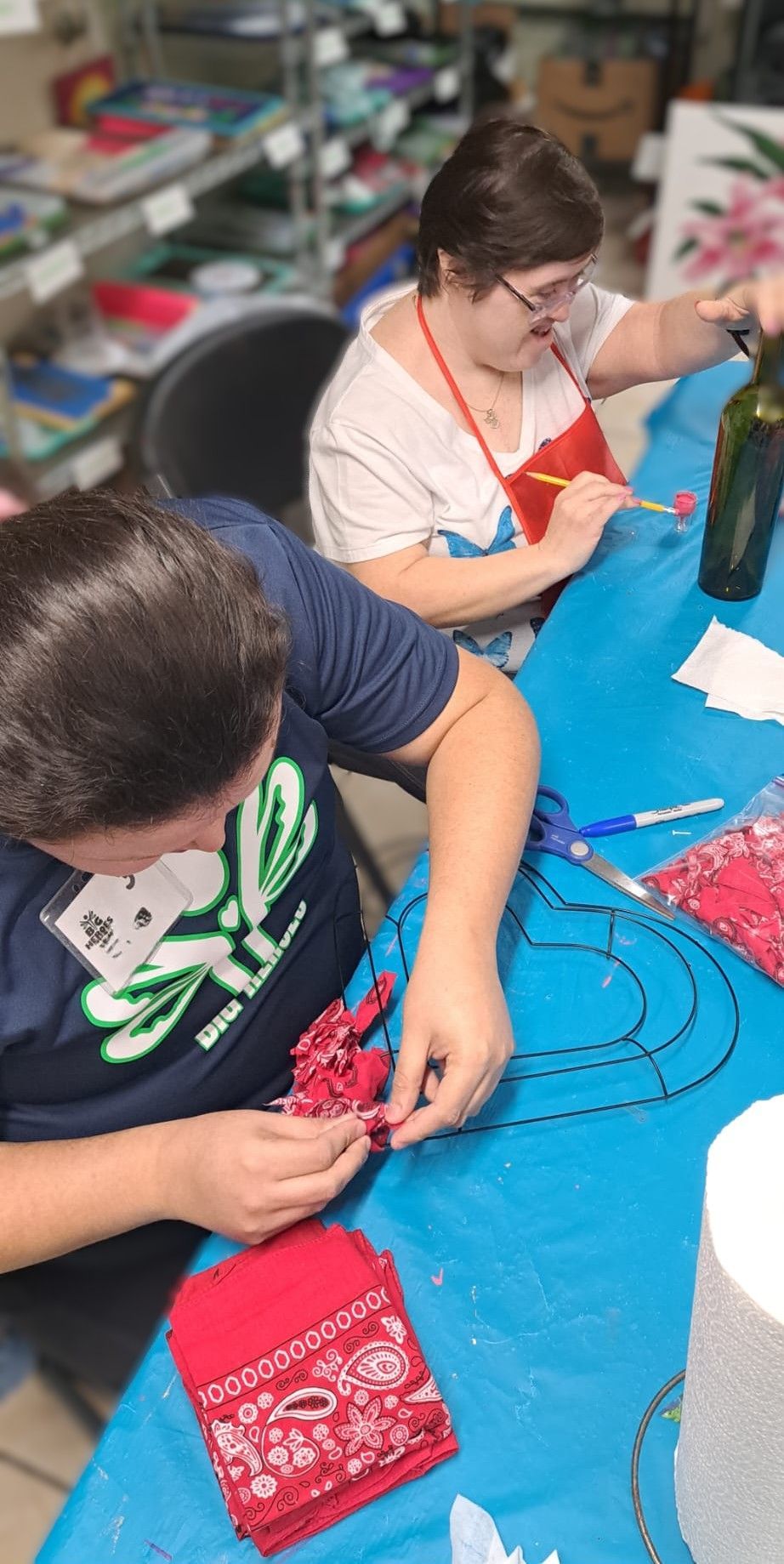 A group of people are sitting at a table making a wreath.