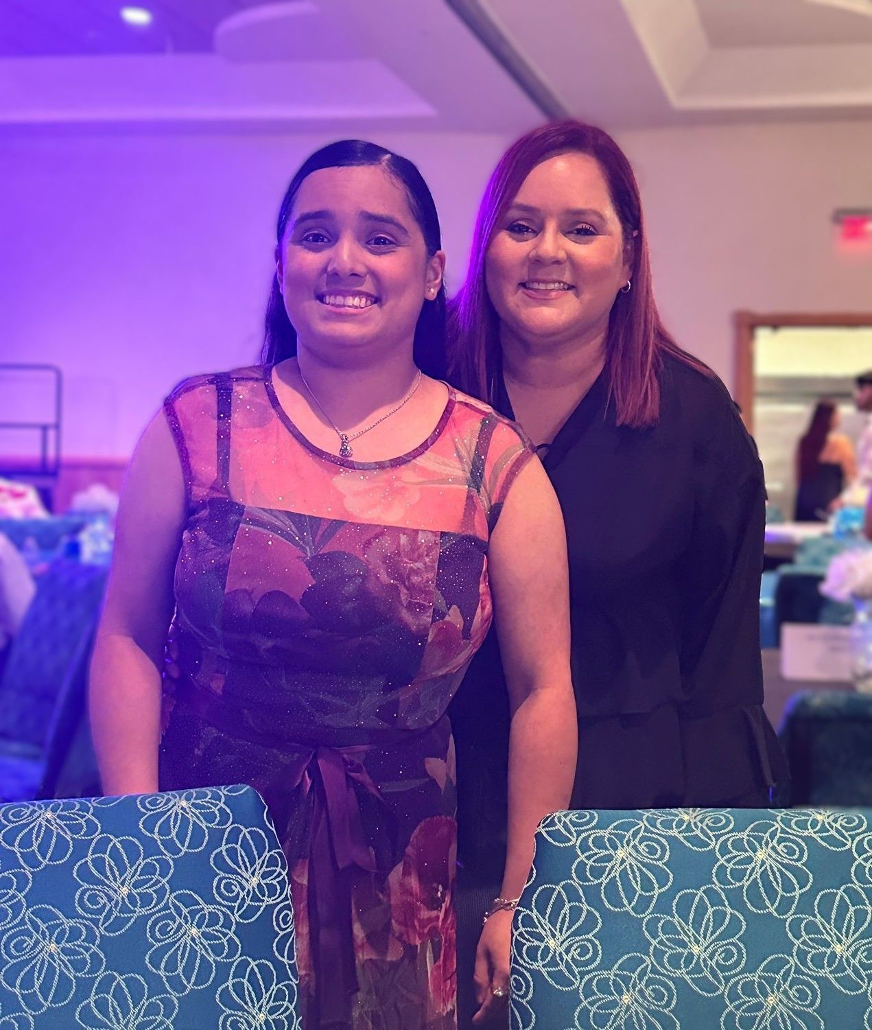 Two women are posing for a picture in a room with purple lights