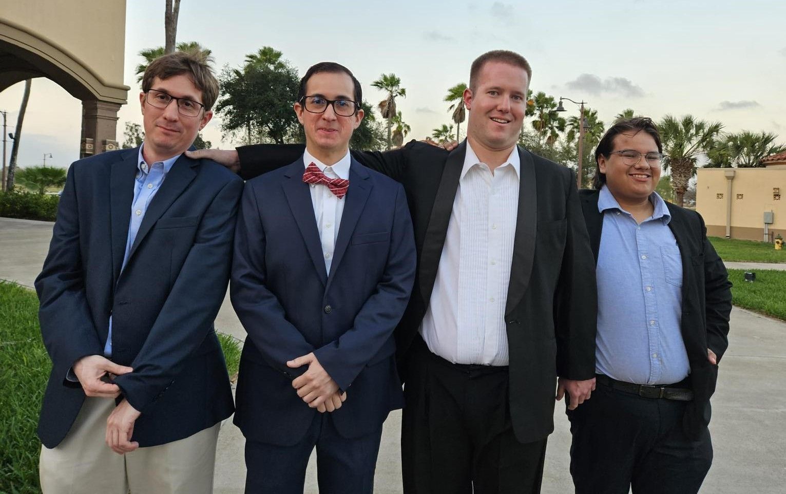 Four men in suits and bow ties are posing for a picture.