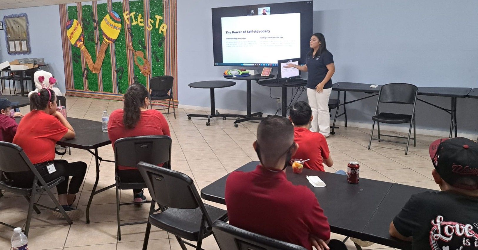 A woman is giving a presentation to a group of people sitting at tables.