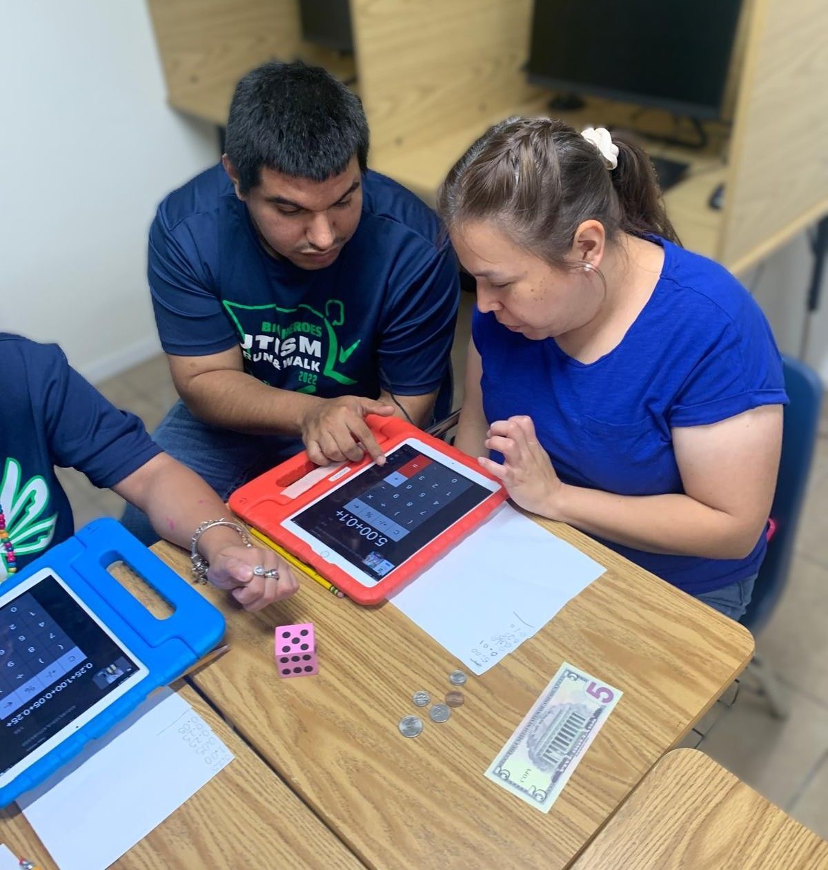 A group of people are sitting at a table with a tablet and a 5 dollar bill