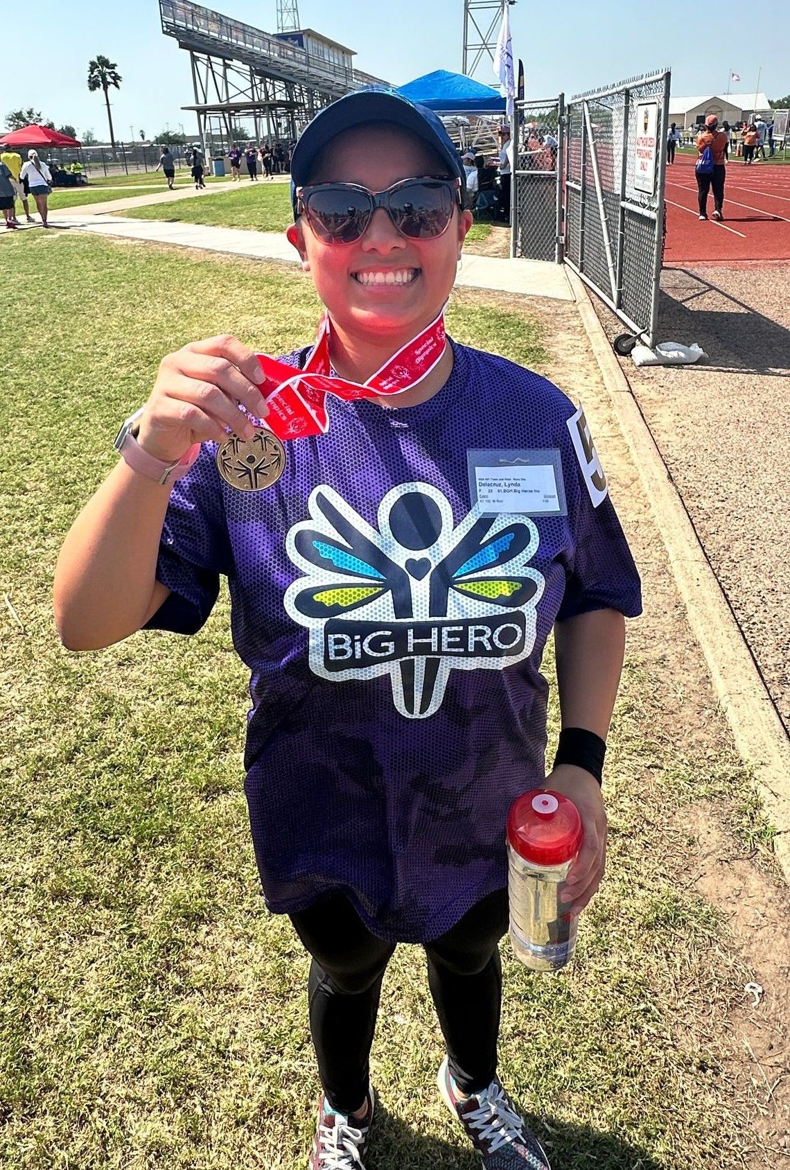 A woman in a purple shirt is holding a medal and a water bottle.