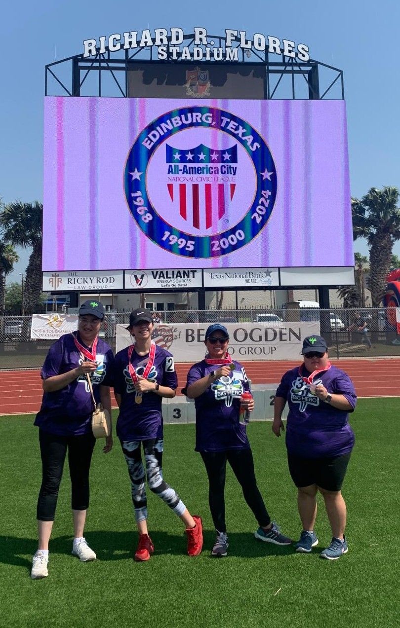 A group of people are standing on a field in front of a large screen.