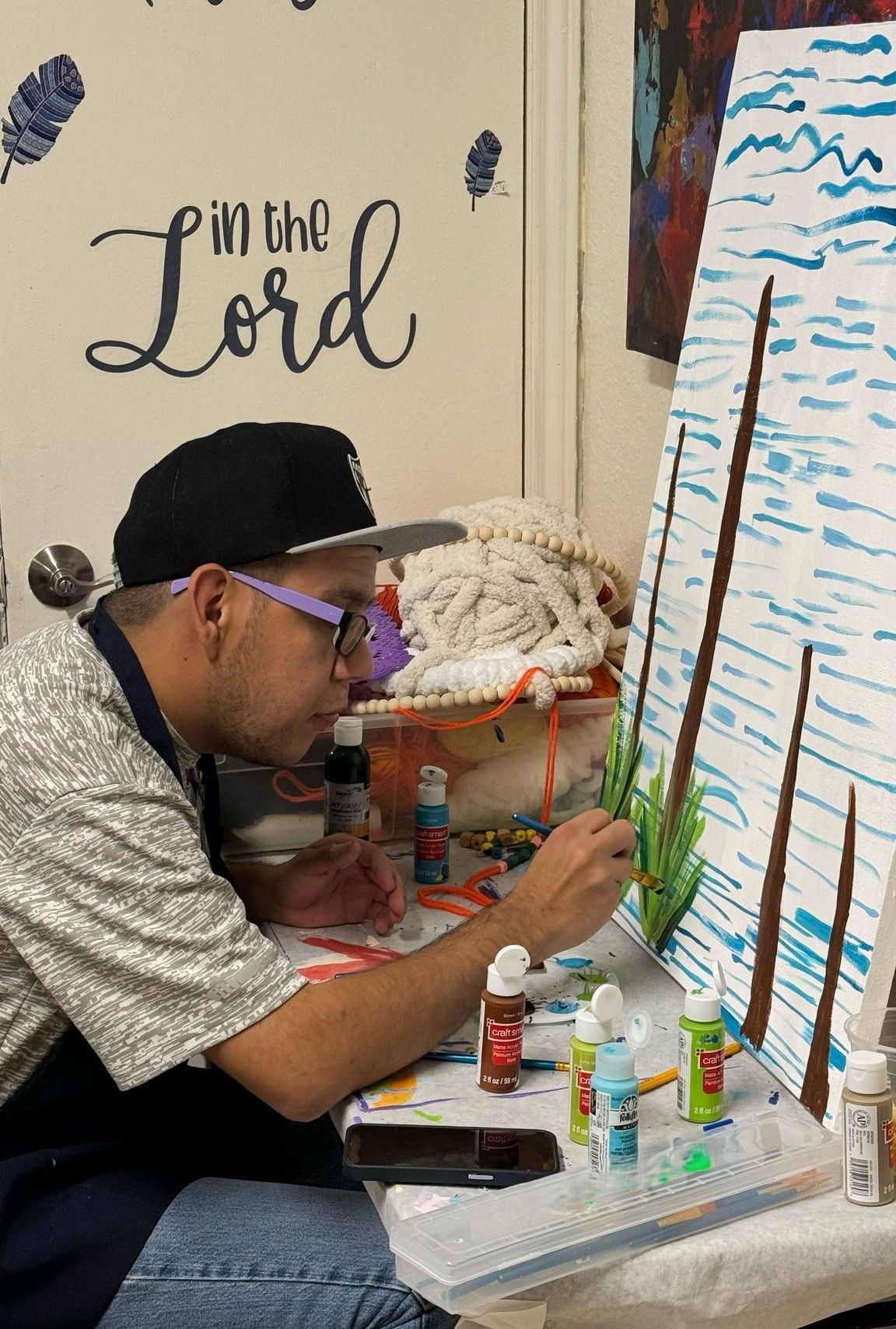 A man is sitting at a table painting on a canvas.