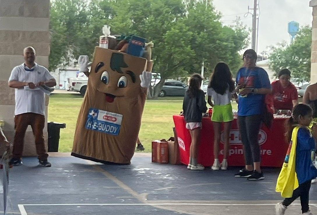 A group of people are standing around a cardboard bag mascot.
