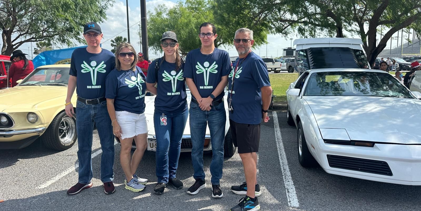 A group of people are posing for a picture in front of cars in a parking lot.