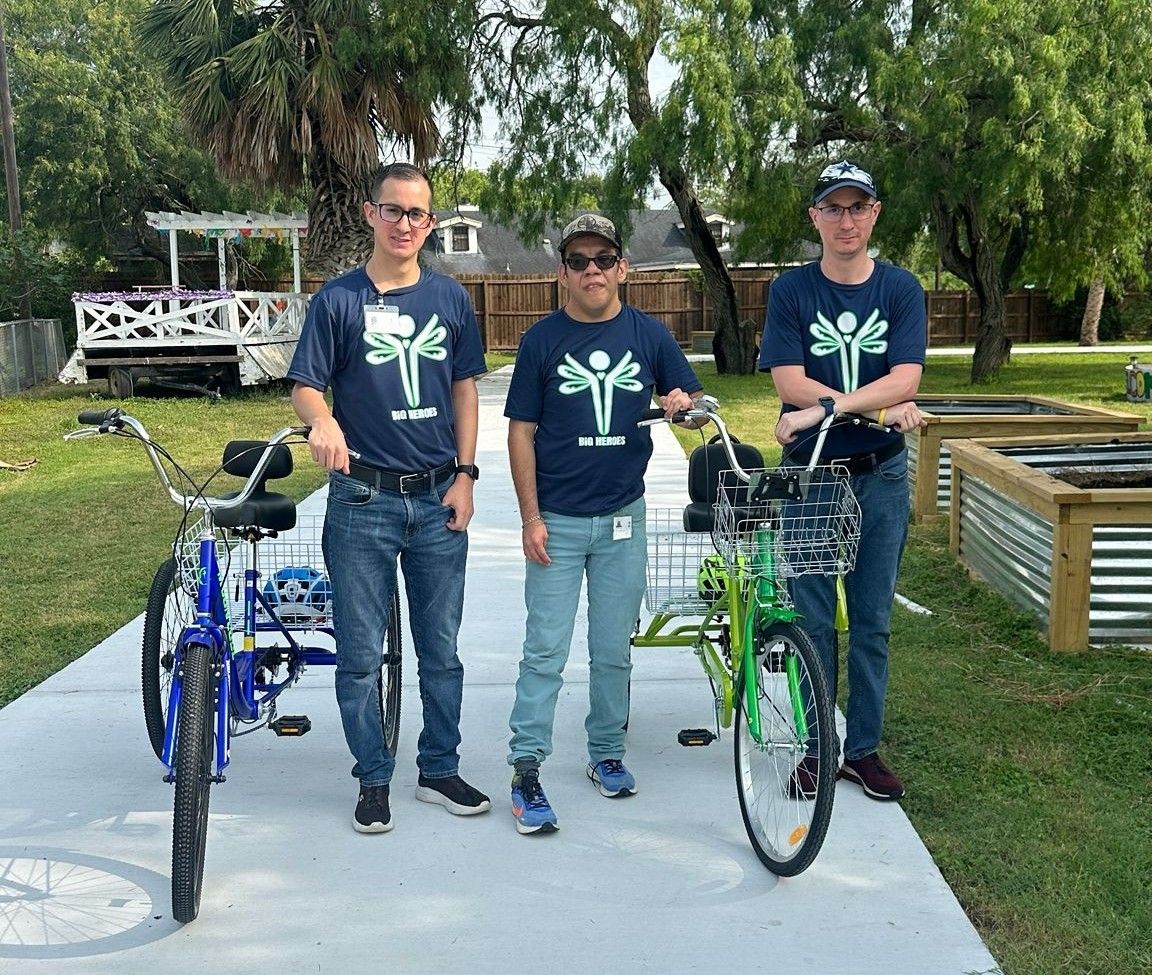 Three men are standing next to bicycles on a sidewalk