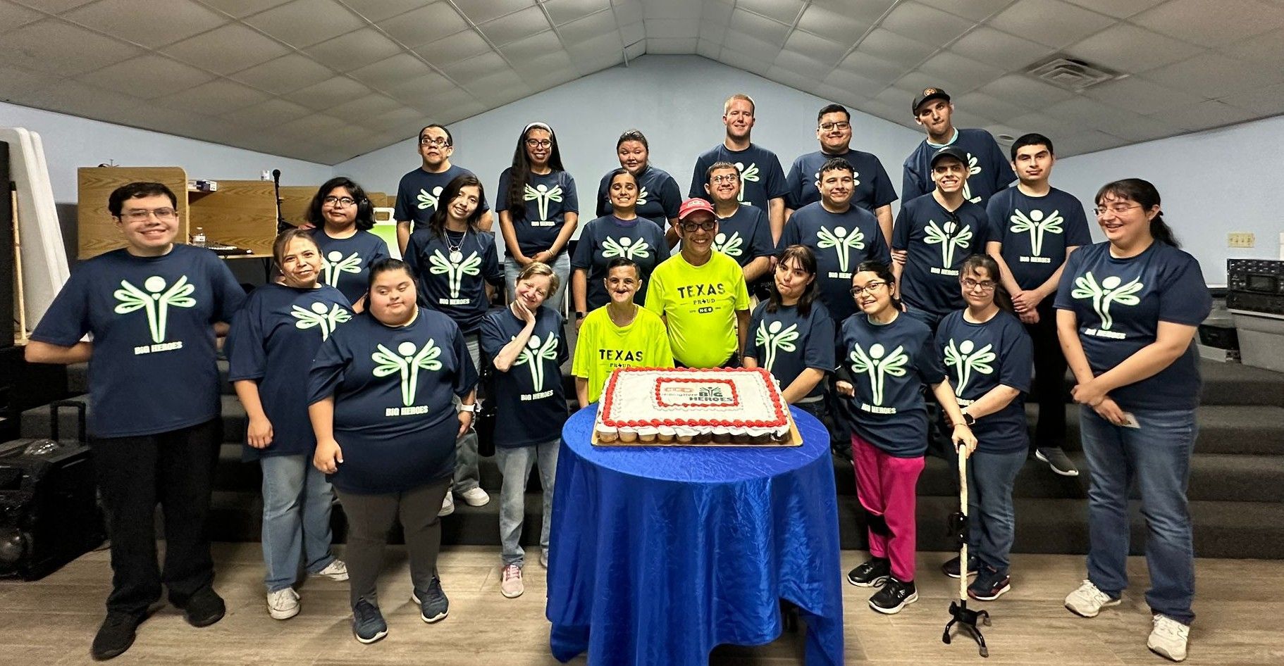 A group of people are standing around a table with a cake on it.