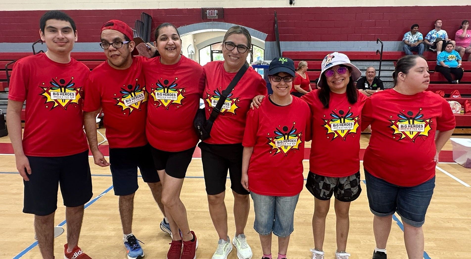 Group of people in red team shirts posing on a basketball court.