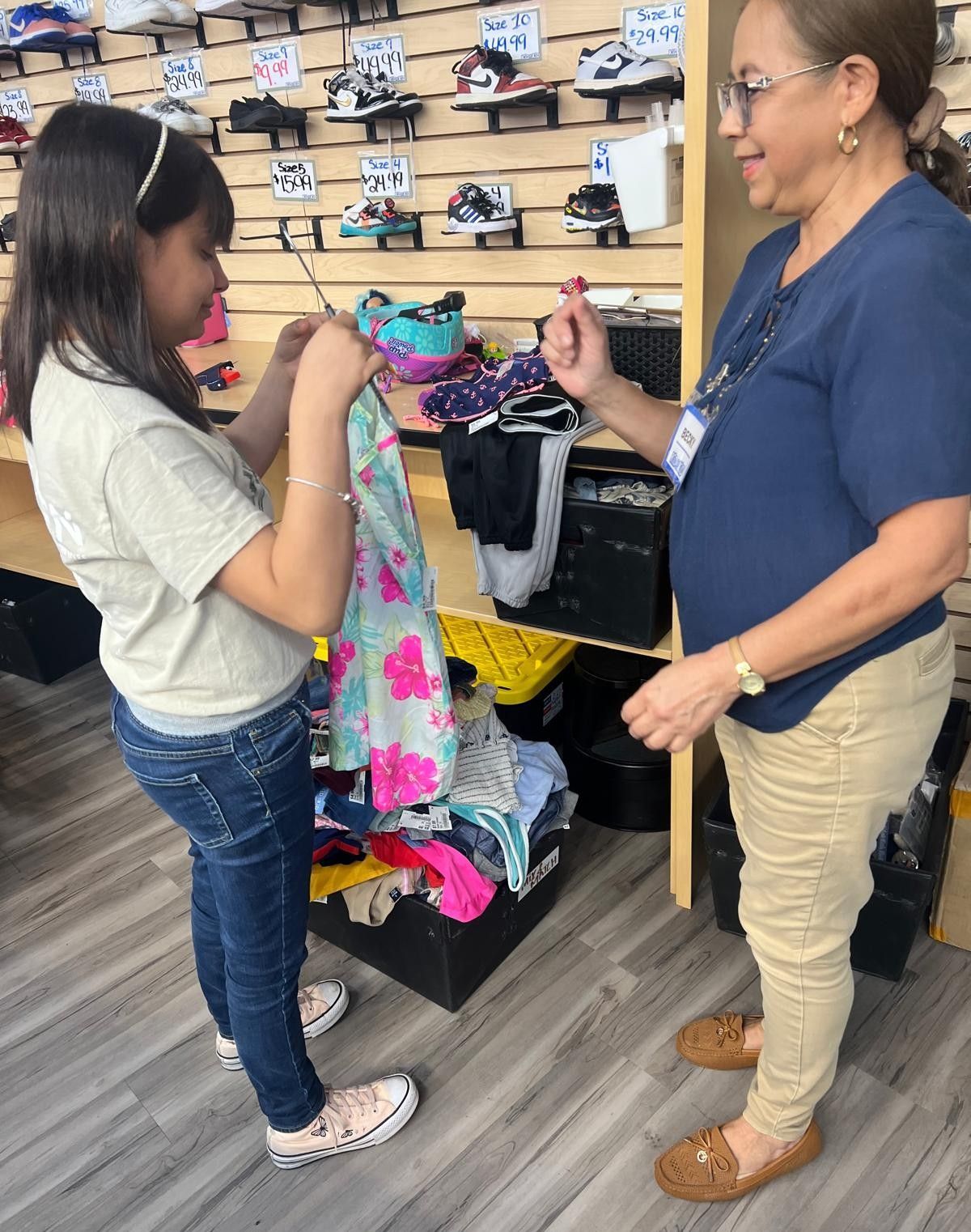 Girl holding a dress, shopping with a woman in a store with shoes on display.