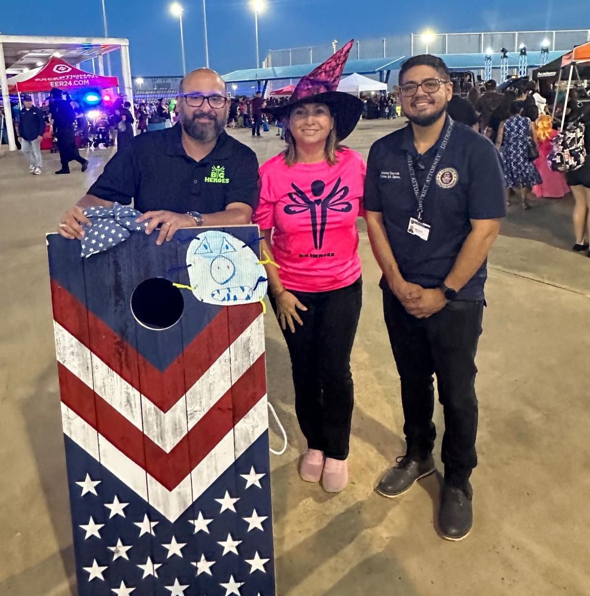 A woman in a witch hat is standing next to two men