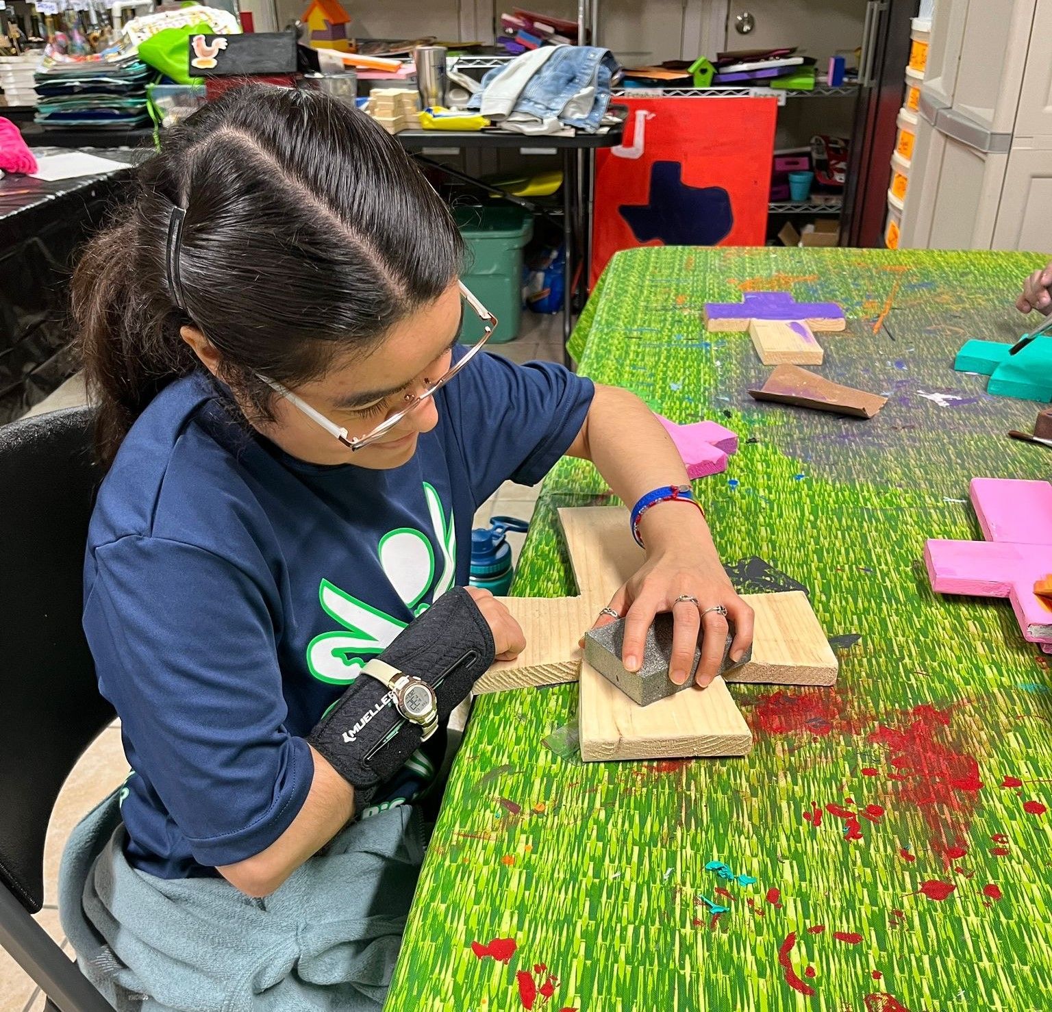 A woman is sitting at a table working on a piece of wood.