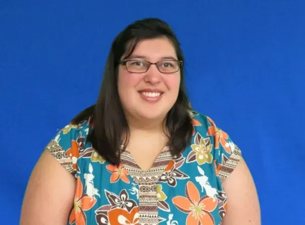 A woman wearing glasses and a floral shirt smiles for the camera
