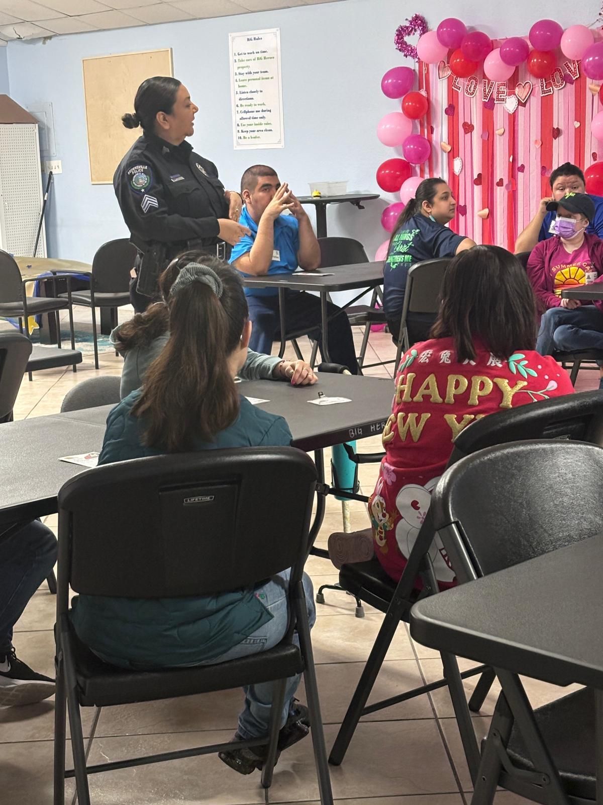 A woman in a police uniform is talking to a group of people sitting at tables.
