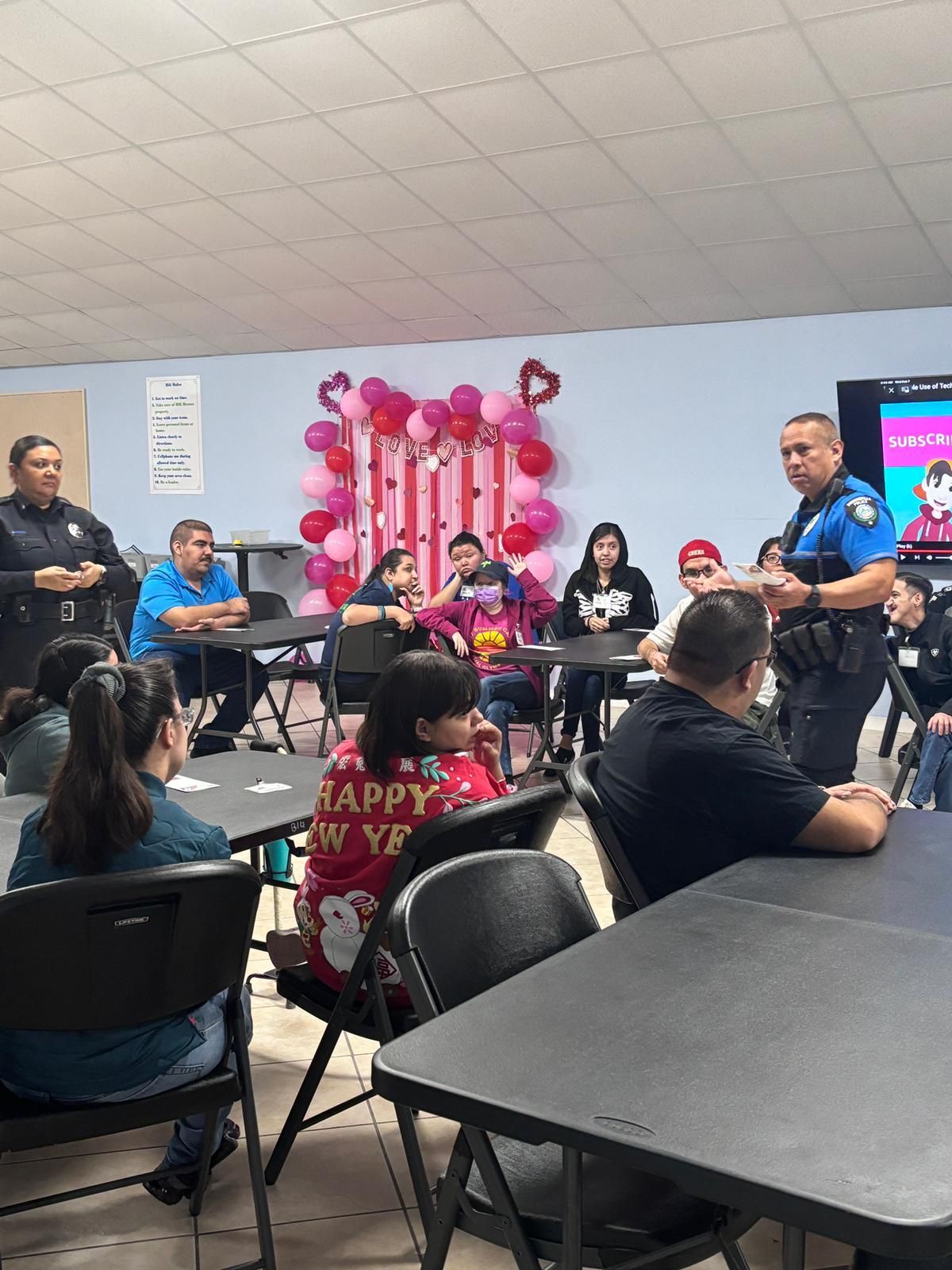 A group of people are sitting at tables in a room with balloons on the wall.