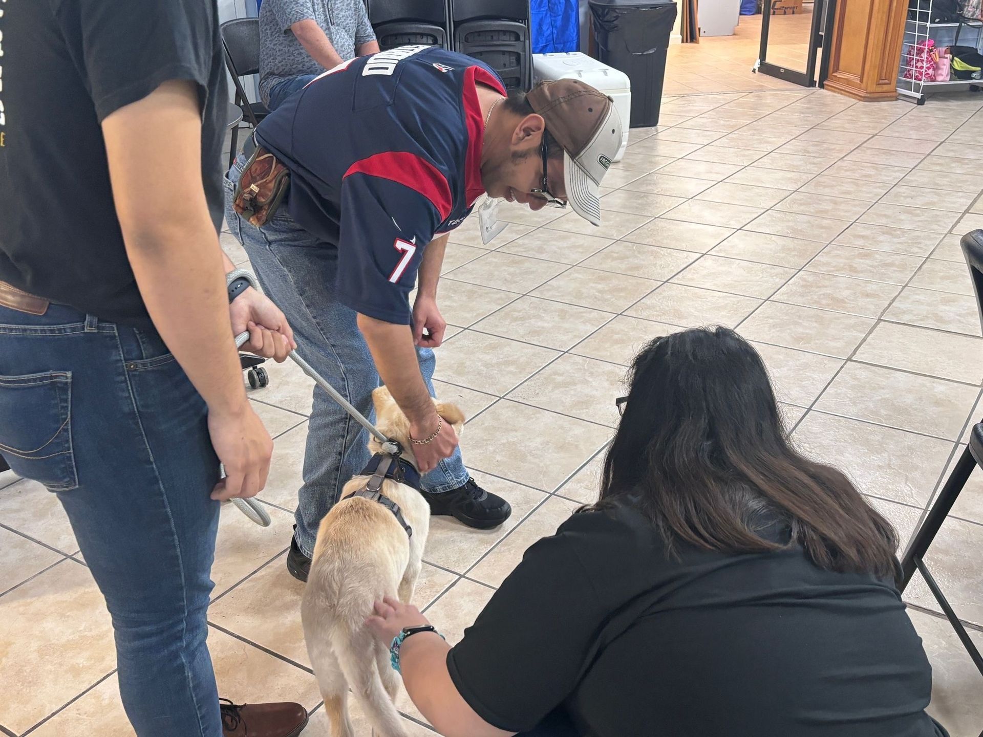 A man in a texans jersey is petting a dog while a woman looks on.