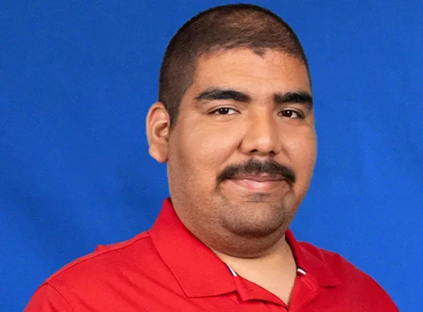 A man with a mustache is wearing a red shirt and smiling.