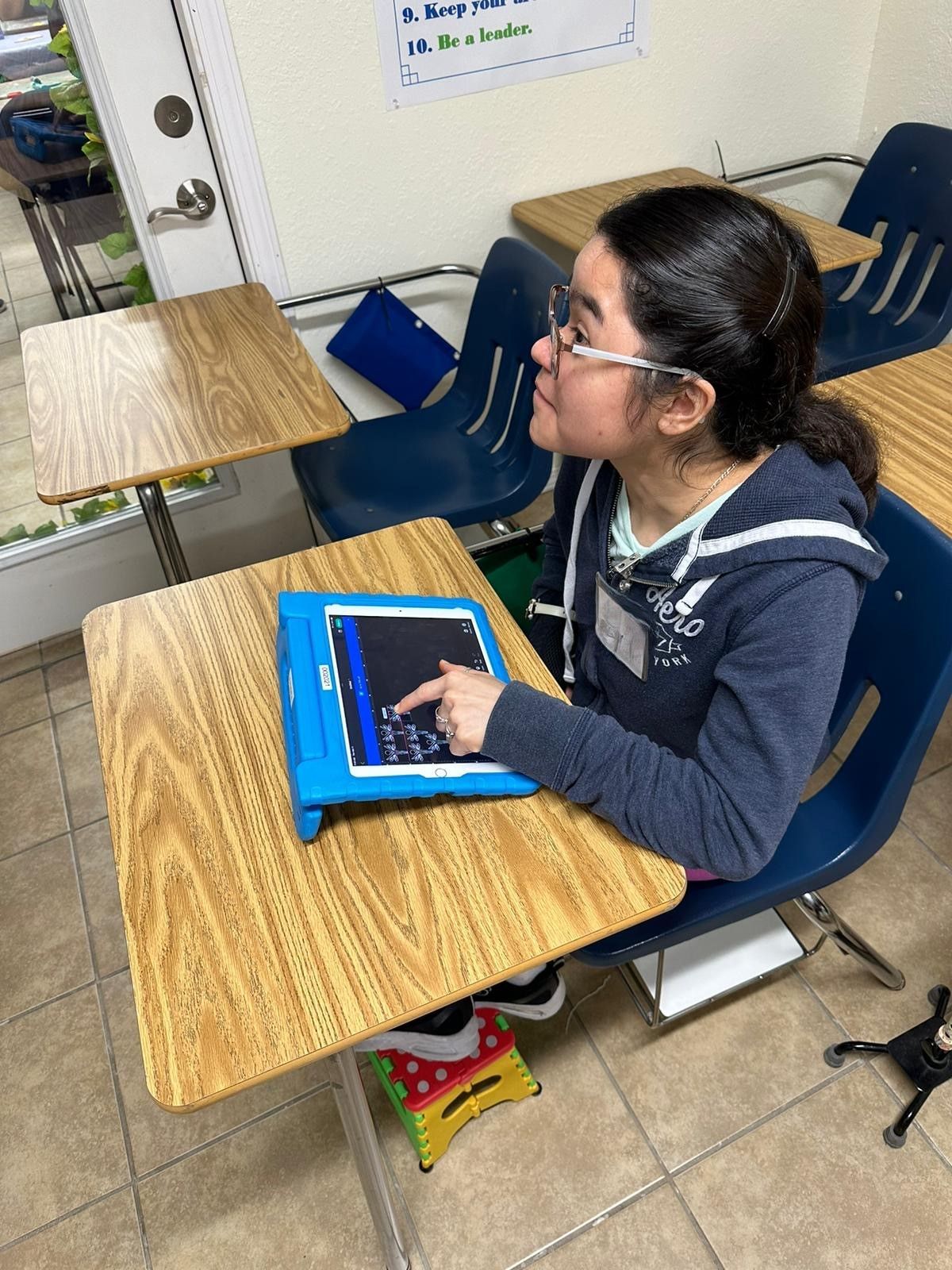 A girl is sitting at a desk in a classroom using a tablet computer.