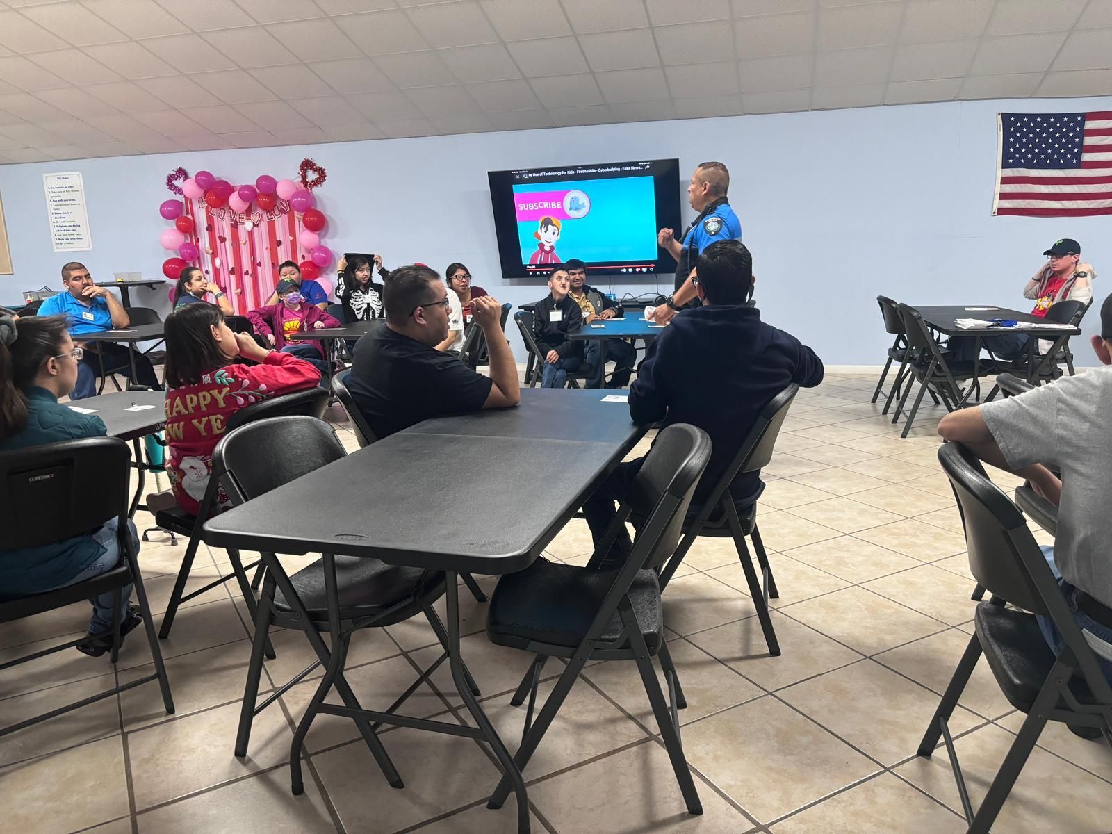 A group of people are sitting at tables in a room with an american flag on the wall.