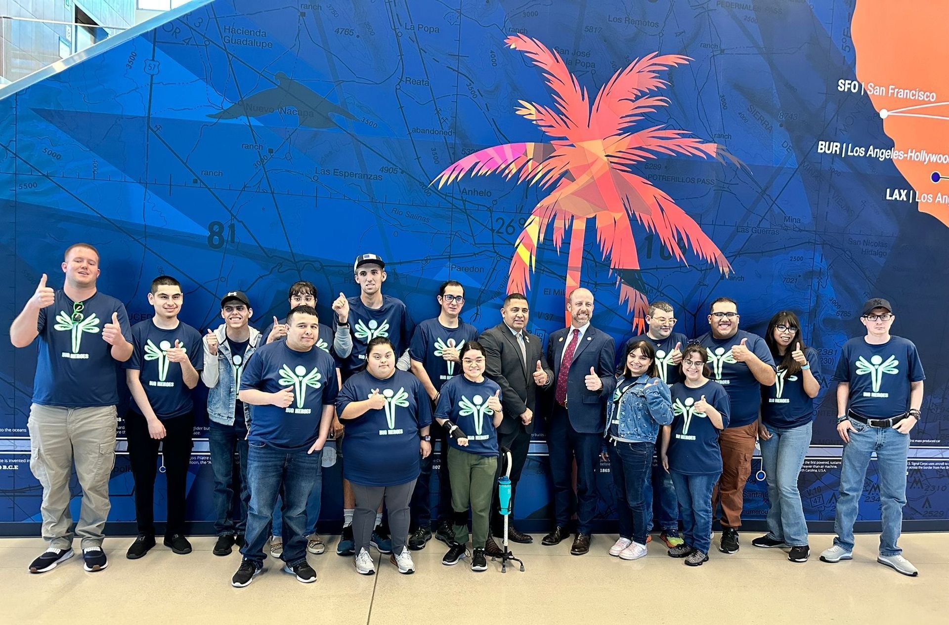 A group of people are posing for a picture in front of a wall with a palm tree on it.