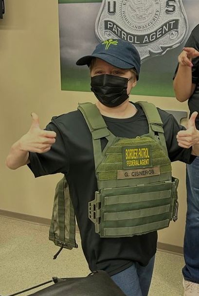 A person wearing a mask and a patrol agent vest giving a thumbs up