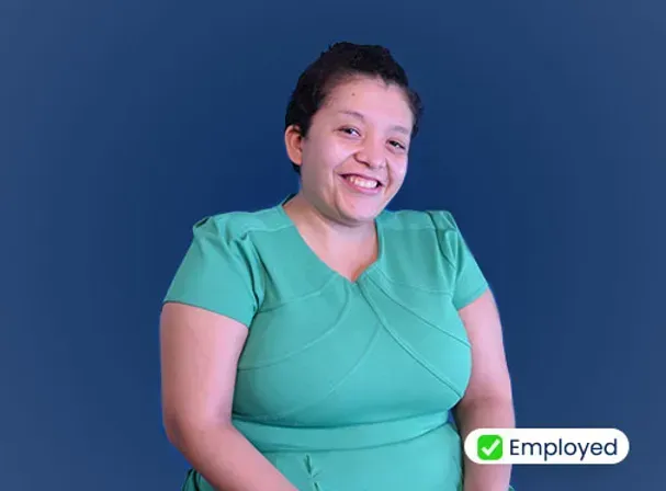A woman in a green dress is smiling in front of a blue background.
