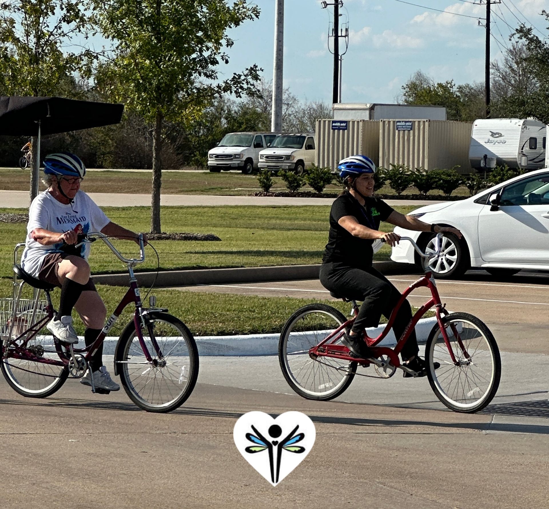 Two people are riding bicycles down a street with a white car in the background