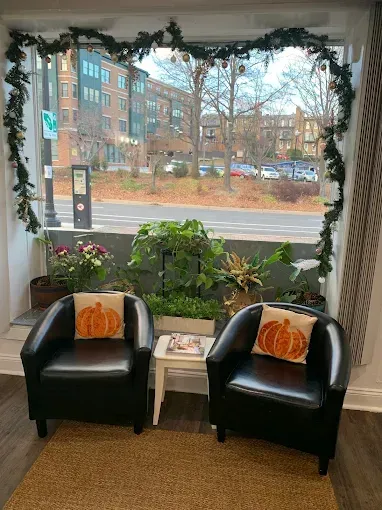 Two black armchairs with pumpkin pillows, near a window decorated with greenery and overlooking a city street.