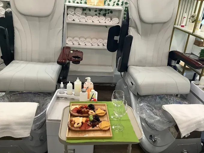 Two pedicure chairs with a snack tray, towels, and shelving unit.