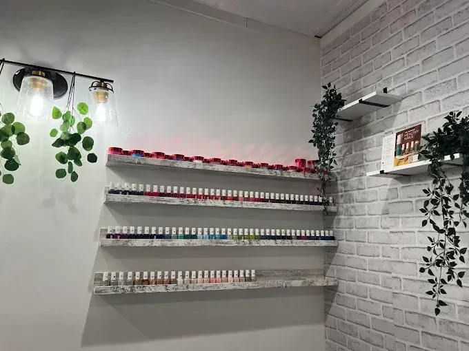 Nail polish bottles displayed on shelves against a white brick wall in a nail salon. Artificial greenery hangs around.