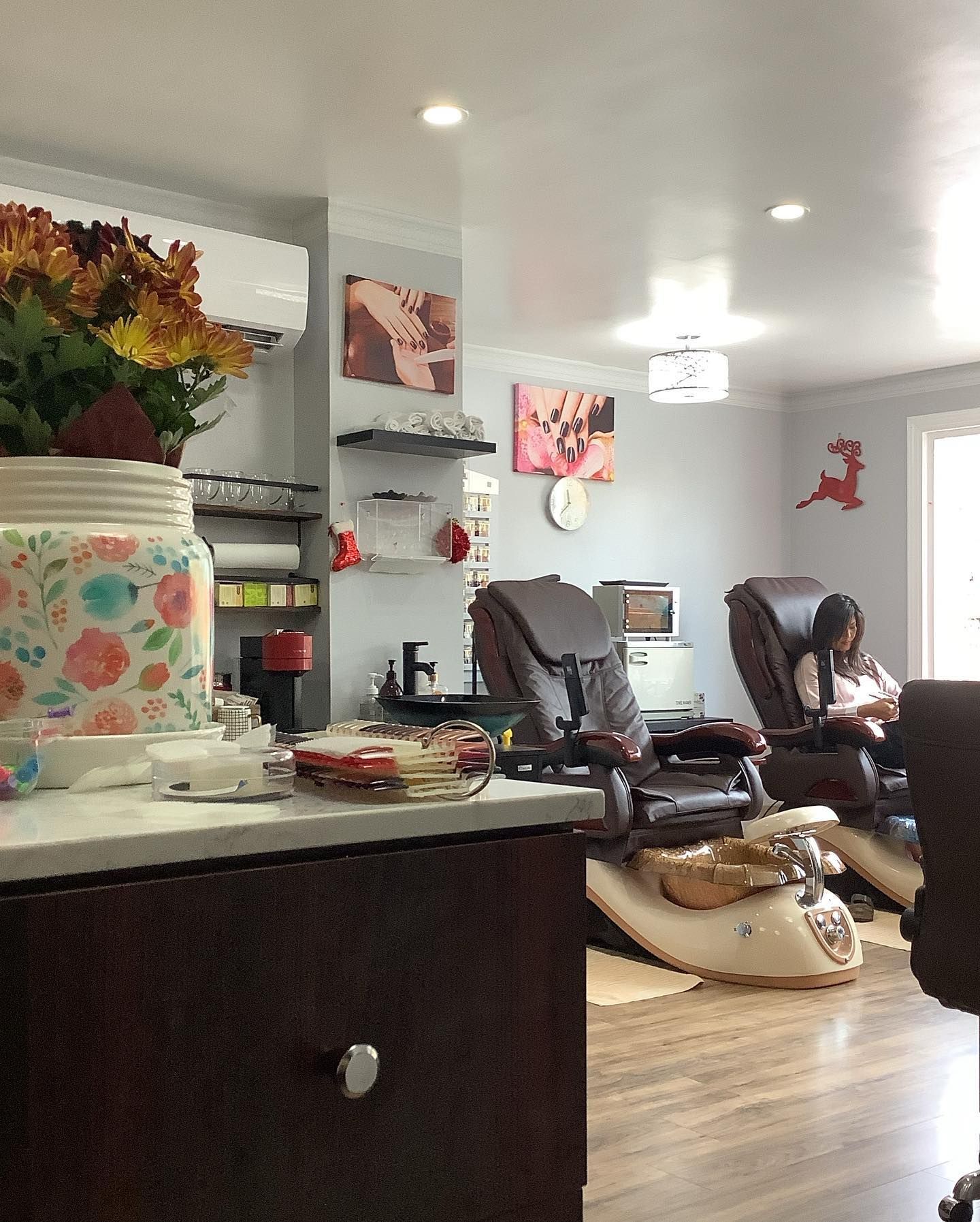 Interior of a nail salon with massage chairs, floral decorations, and a person getting a service.