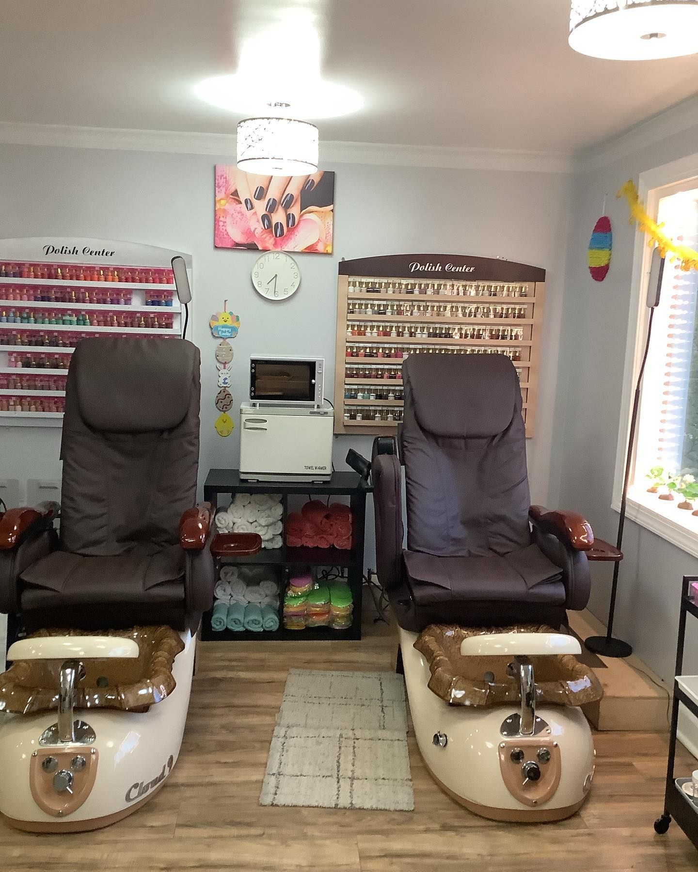 Two massage chairs in a nail salon with manicure supplies and a light above.