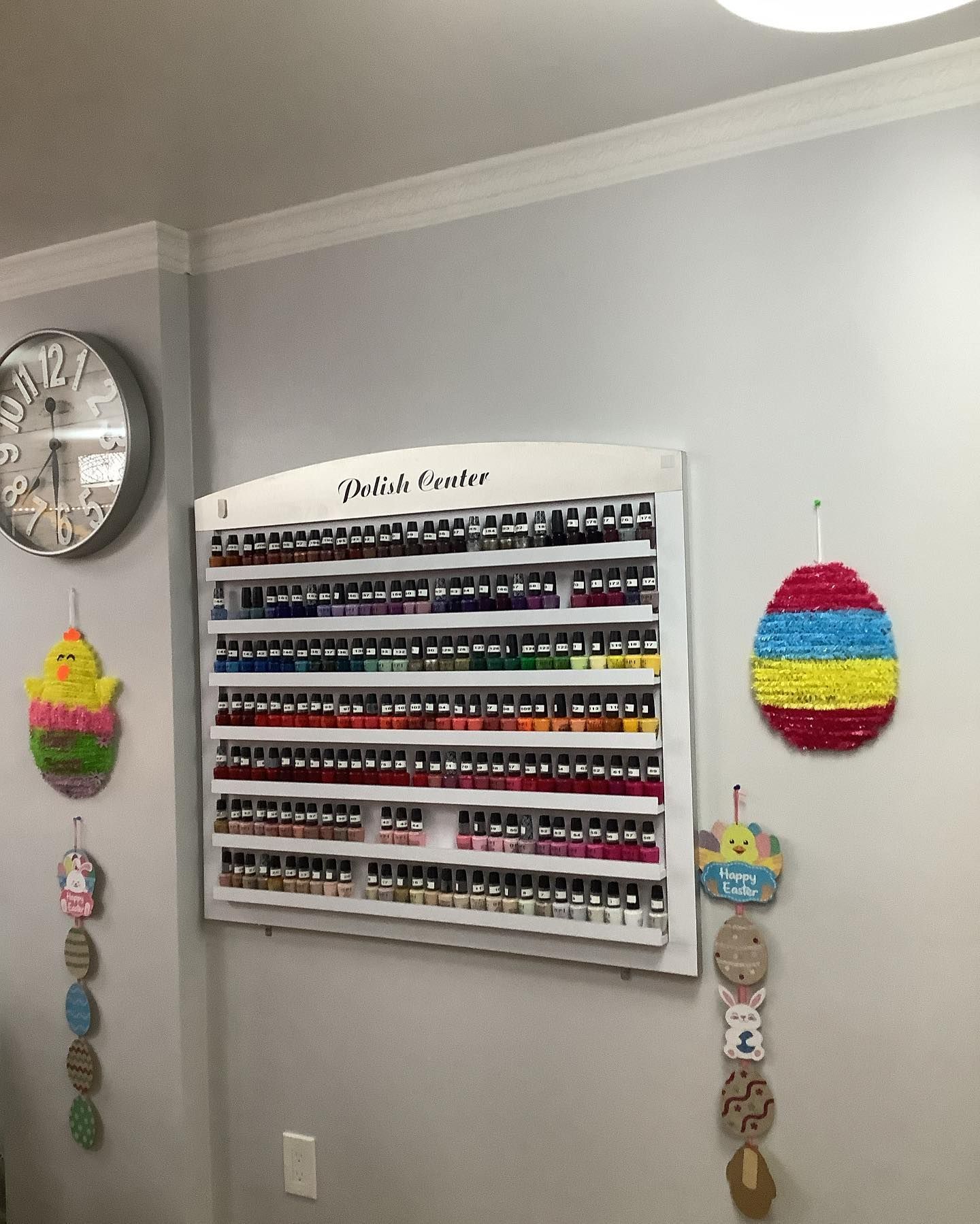 Nail polish display on a wall. Easter decorations, a clock, and a light fixture are also present.
