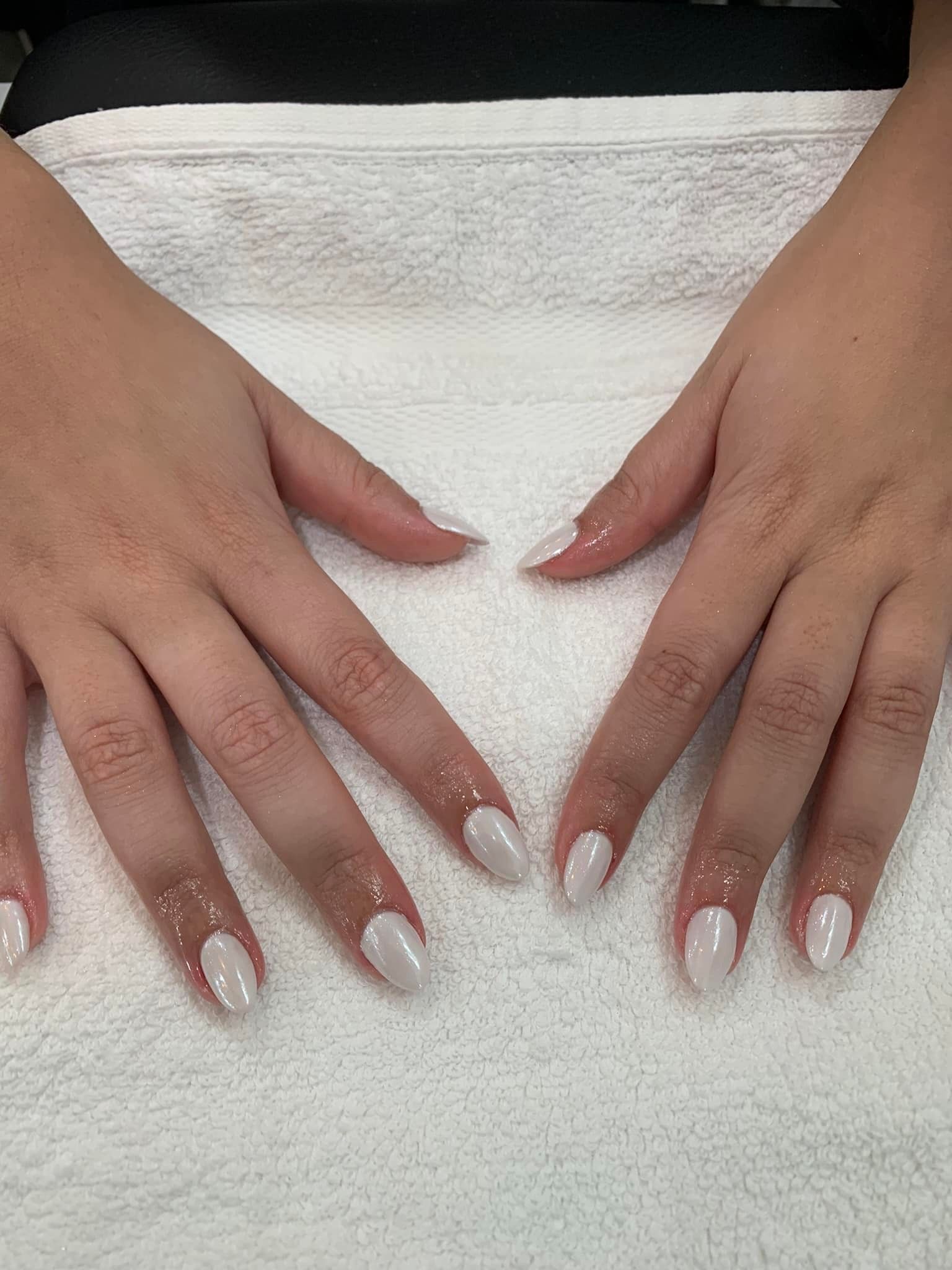 Hands with almond-shaped nails painted white, resting on a white towel.